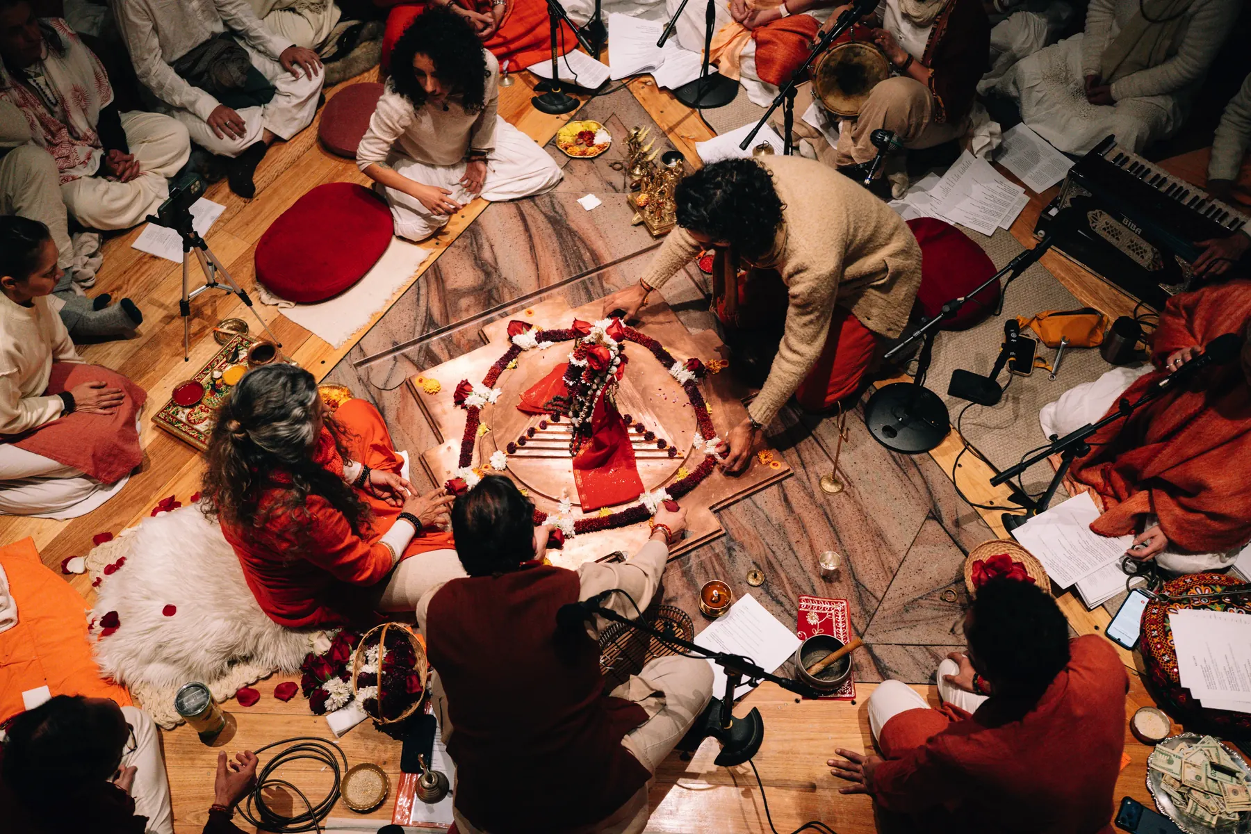 Vista desde arriba de una ceremonia: varias personas alrededor de un yantra de pétalos rojos sobre el suelo de madera