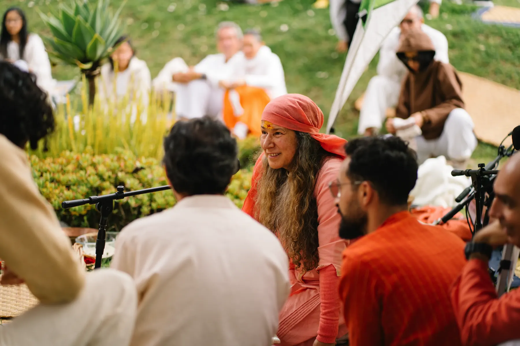 Una mujer con pañuelo rojo sonríe entre un grupo de personas sentadas al aire libre