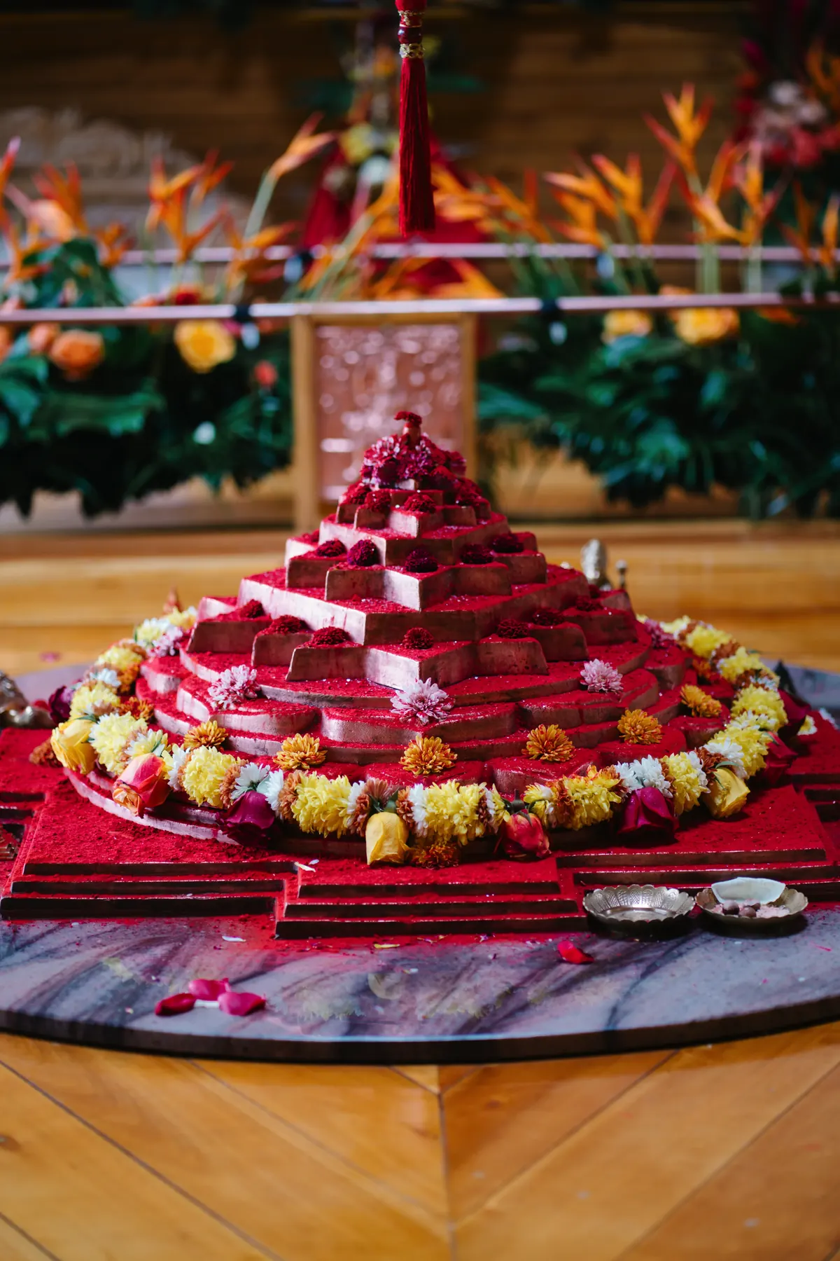 Pirámide de ofrendas rojas rodeada de guirnaldas de flores sobre una mesa redonda