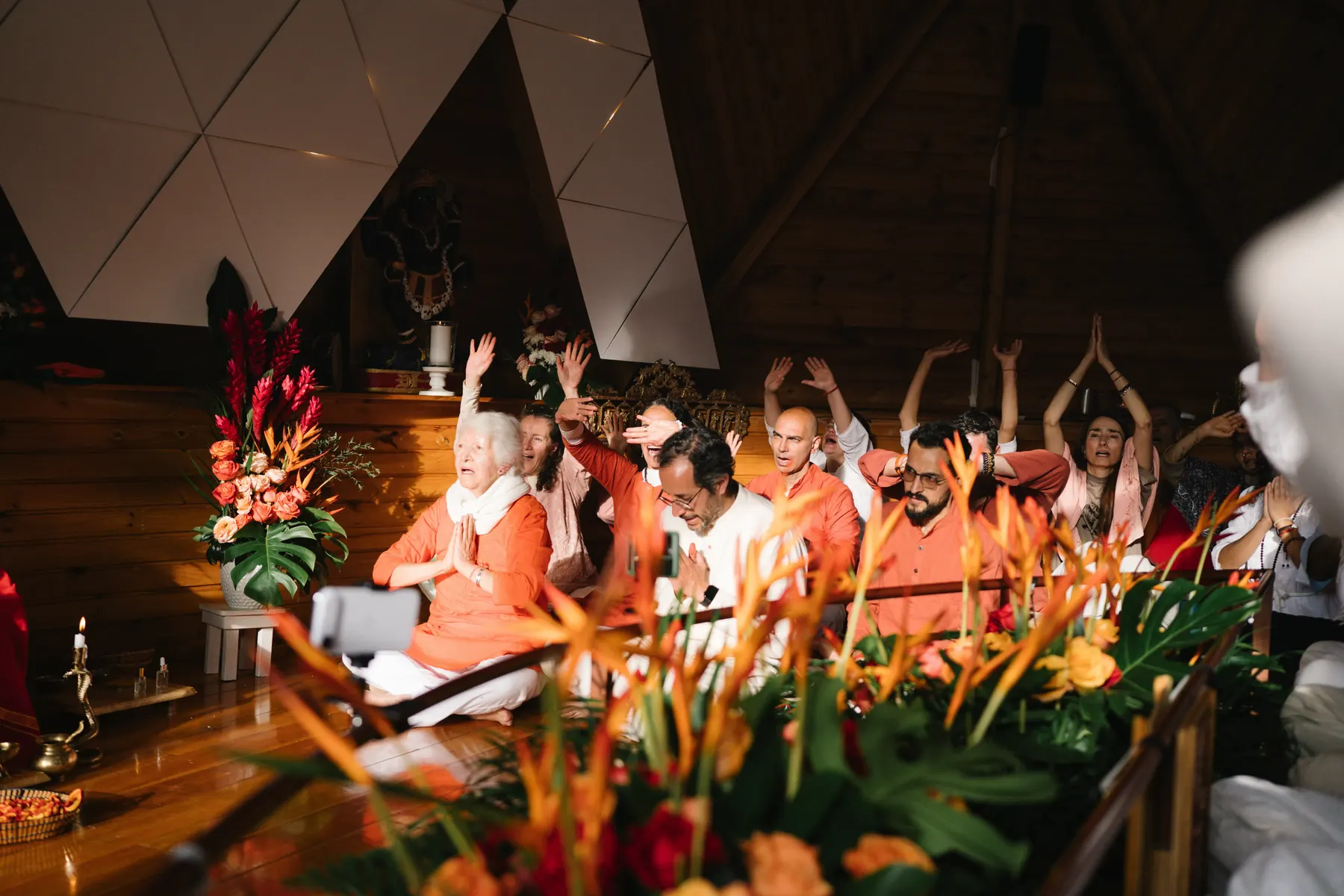 Personas sentadas con los brazos en alto frente a un altar con flores naranjas y rojas