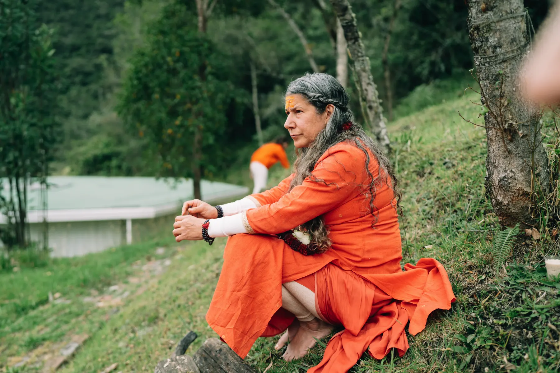 Una mujer vestida de naranja sentada en una ladera, mirando hacia el valle