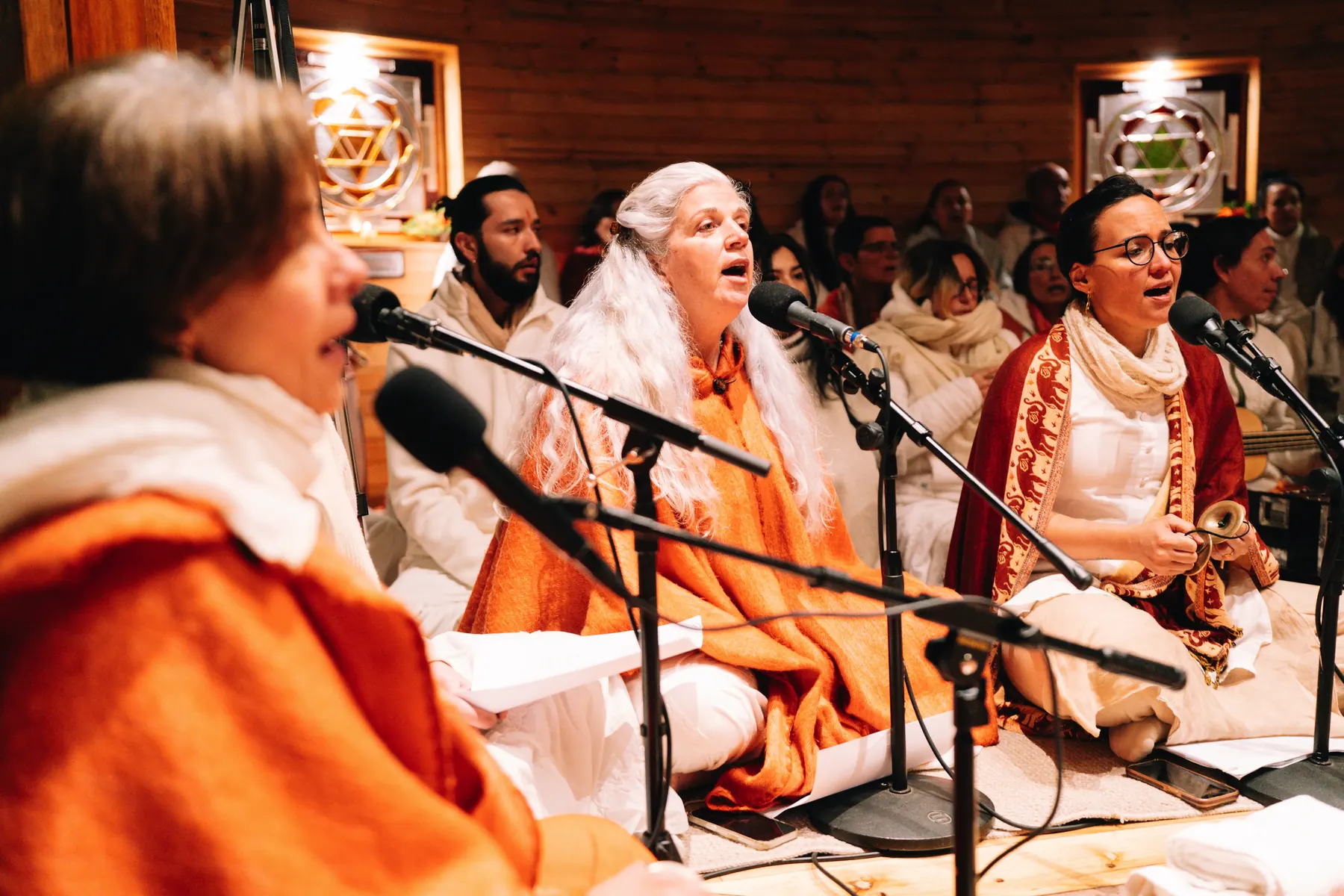 Tres mujeres cantan frente a los micrófonos durante el kirtan