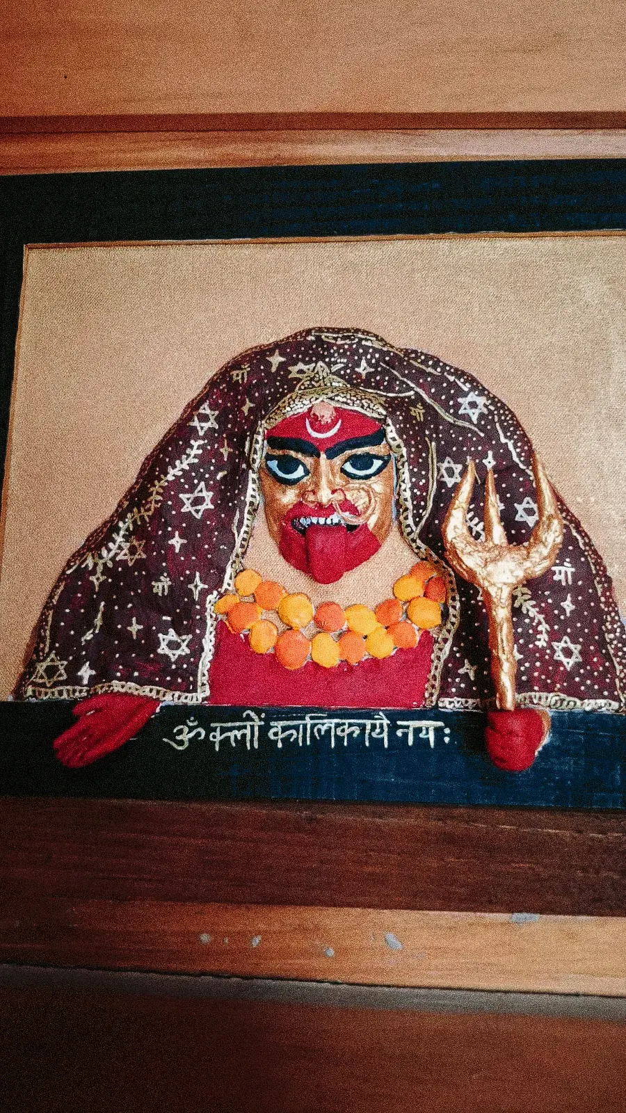 Rostro de Mahakali hecho a mano en relieve y pintado, con manto de estrellas, guirnalda de caléndulas, tridente dorado y un mantra escrito en sánscrito