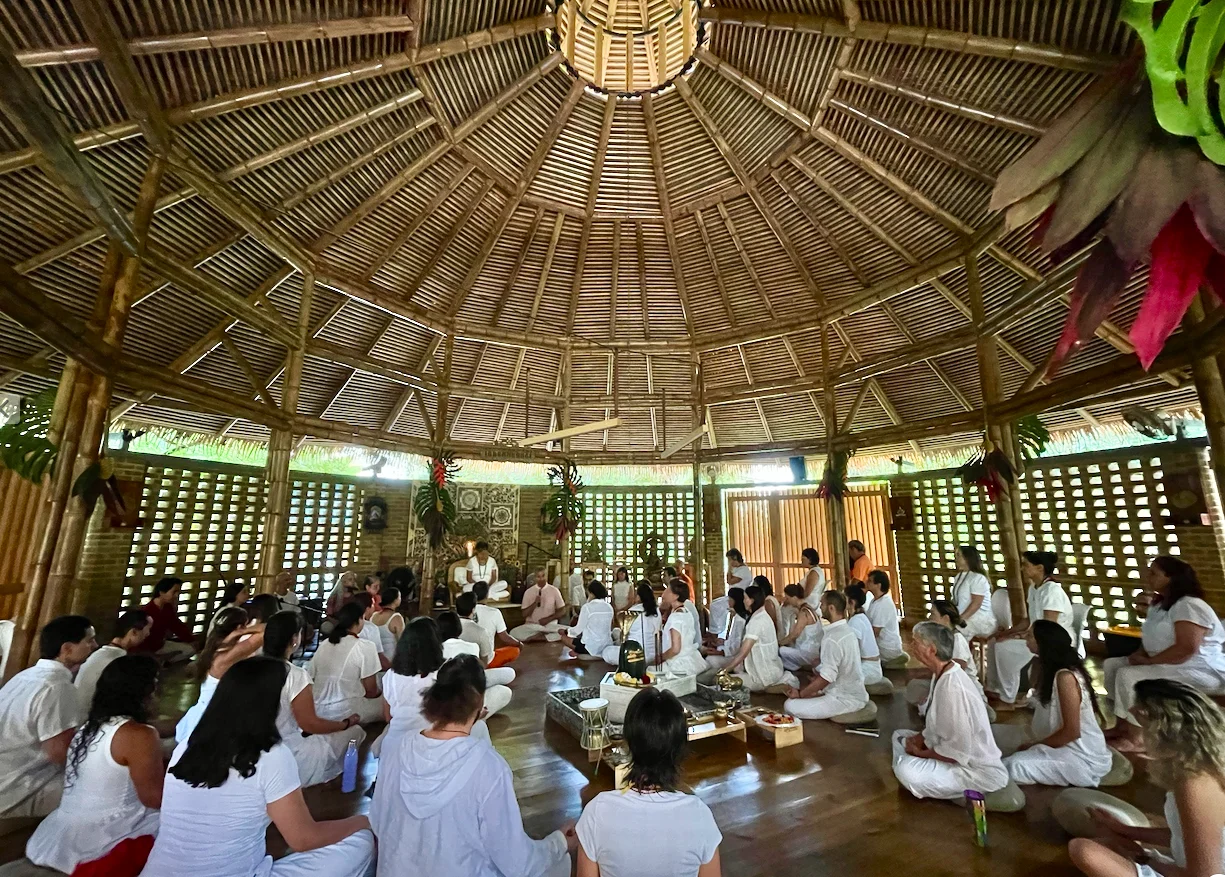 Interior de un templo circular de bambú con techo en cúpula, lleno de participantes vestidos de blanco sentados en el suelo alrededor de un altar