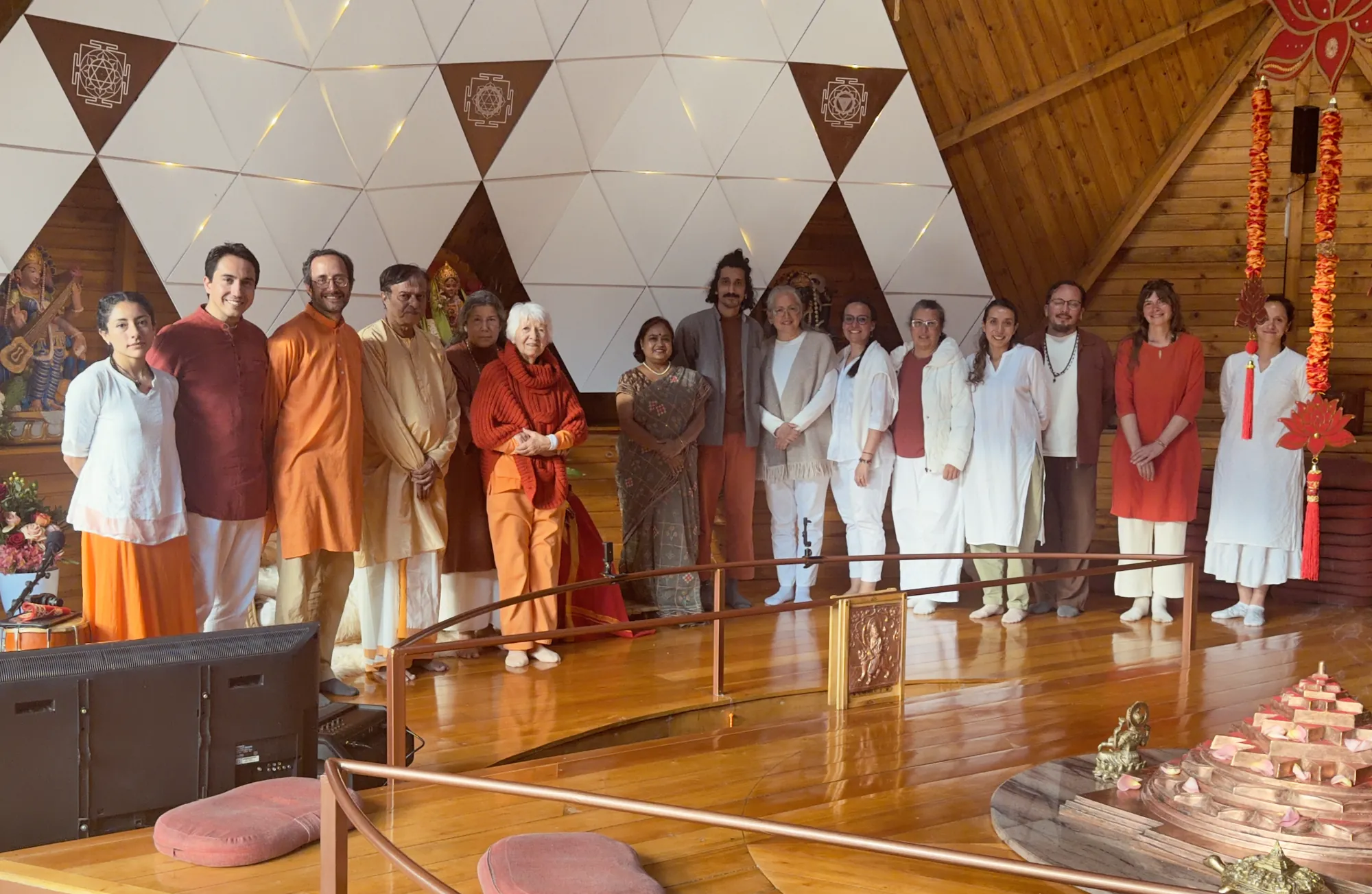 Grupo de visitantes y anfitriones posando juntos en el templo, frente a un muro de triángulos blancos con imágenes de las Devis